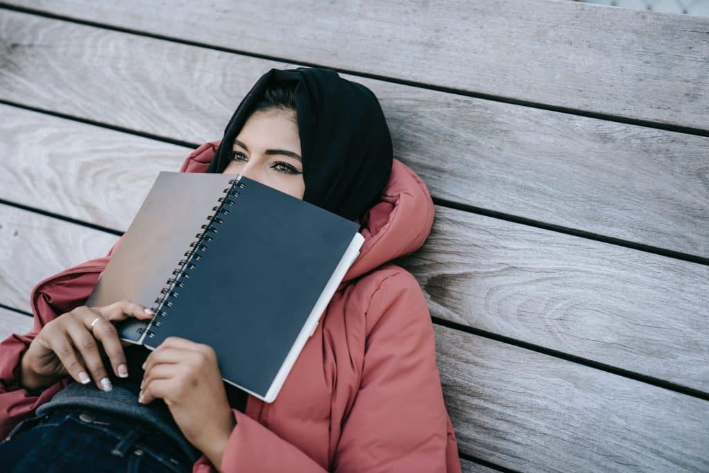 Menina deitada no chão com um livro aberto cobrindo parte do seu rosto