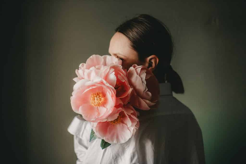 Mulher branca segurando flores rosas.