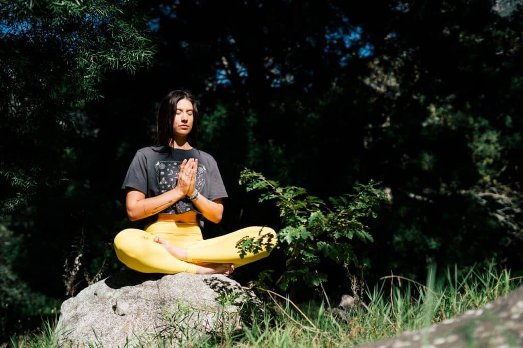 Mulher branca meditando numa pedra.