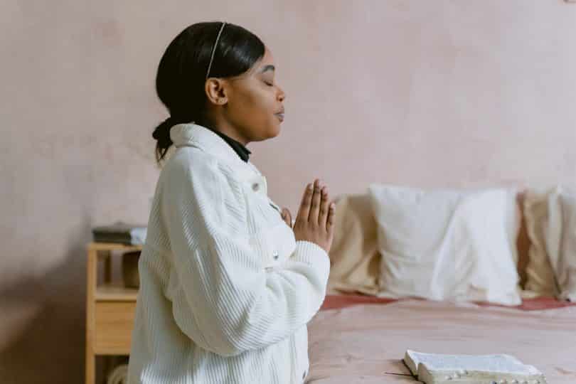 Mulher negra de olhos fechados com as mãos juntas.