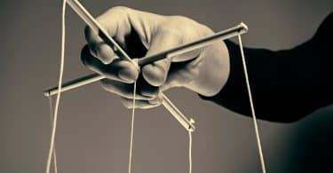 Uma mão manipulando cordas de uma marionete.