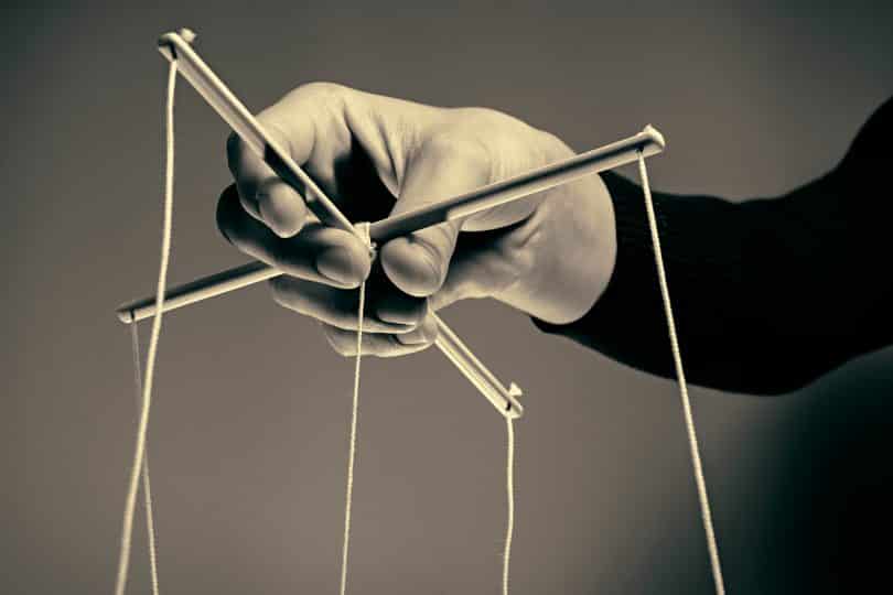 Uma mão manipulando cordas de uma marionete.