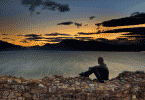 silhueta de homem sentado na praia olhando para o por do sol