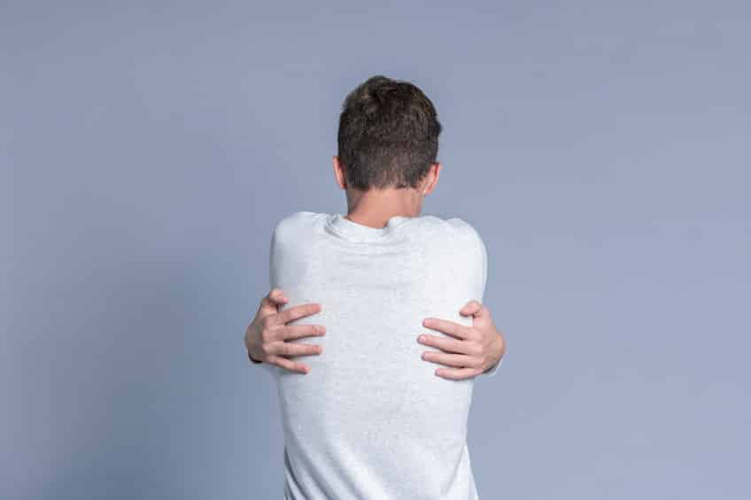 Homem branco de costas se abraçando.