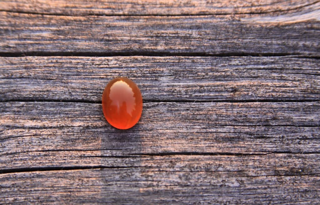 Uma pedra preciosa de ágata laranja isolada em fundo de madeira brilhando à luz do sol. 