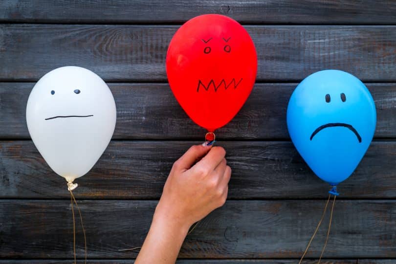Balões com expressões humanas distintas. Um branco, à direita, transparecendo tédio; um vermelho, central, transparecendo receio; um azul, à direita, tristeza