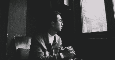 Foto em preto e branco de um homem sentado e olhando pela janela de vidro