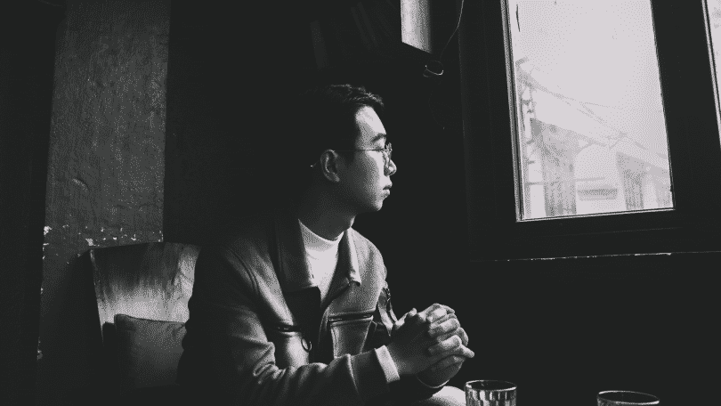 Foto em preto e branco de um homem sentado e olhando pela janela de vidro