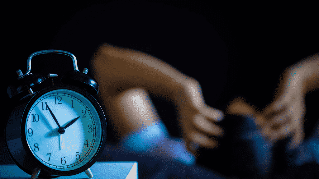 Relógio marcando duas da manhã e pessoa deitada no fundo com as mãos na cabeça