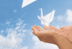 Pessoa com as mãos voltadas para o céu soltando passarinhos de papel