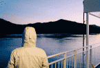 Imagem de uma pessoa de blusa com capuz olhando para um rio