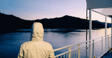 Imagem de uma pessoa de blusa com capuz olhando para um rio