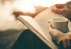 Pessoa segurando xícara de café e lendo um livro