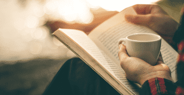 Pessoa segurando xícara de café e lendo um livro