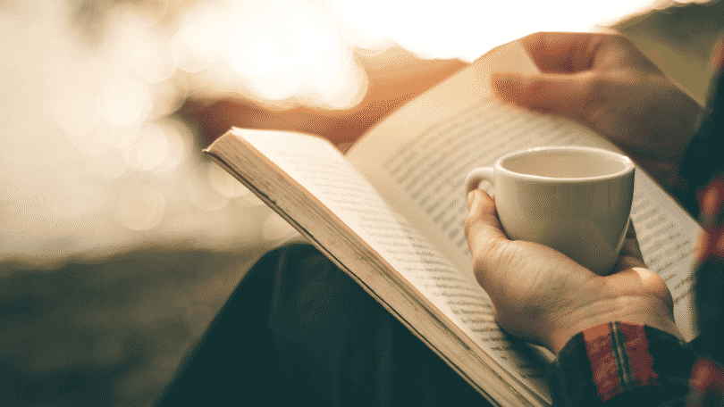 Pessoa segurando xícara de café e lendo um livro