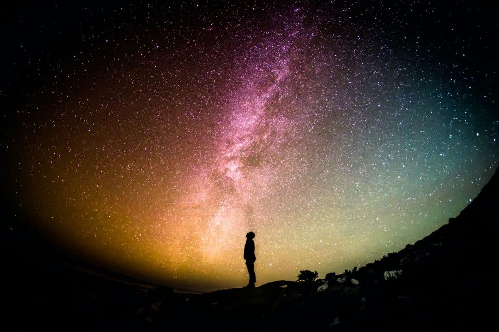 Uma silhueta de um homem contemplando um céu intensamente estrelado.