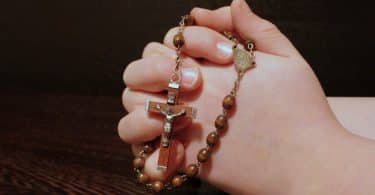 Mãos em gesto de oração segurando um terço.