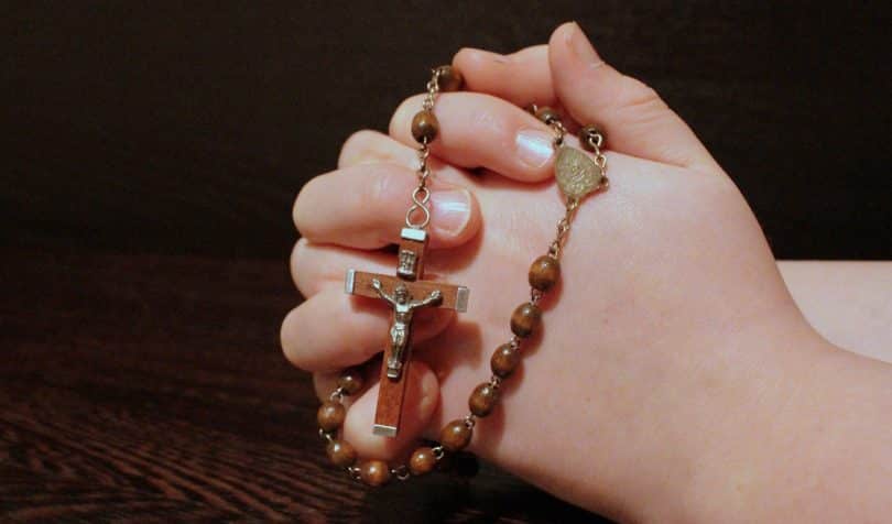 Mãos em gesto de oração segurando um terço.