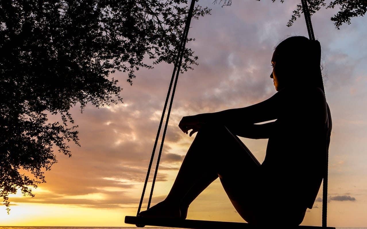 Uma pessoa sentada em um banco balançável de madeira. Ela observa o sol.