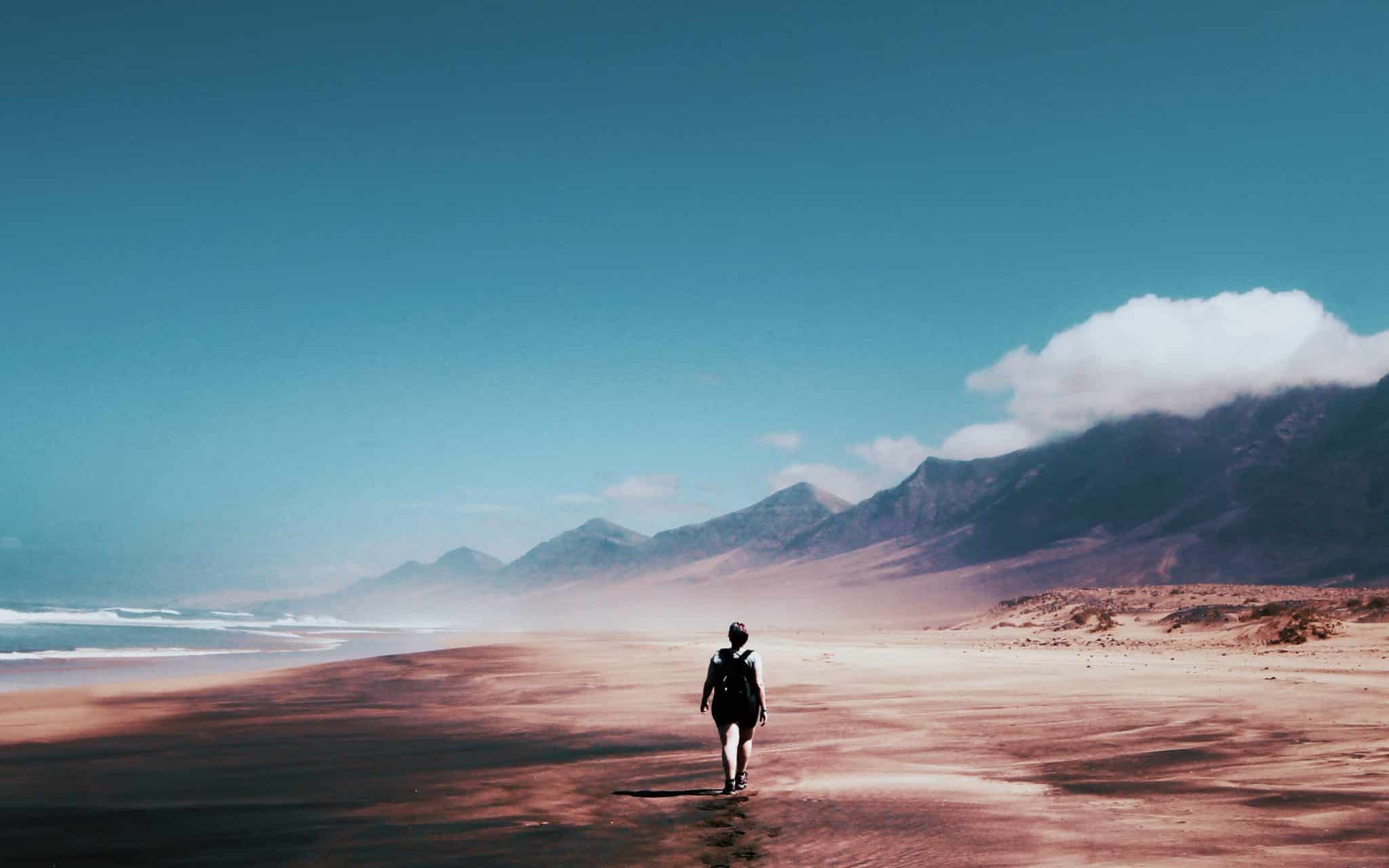 Uma pessoa caminhando numa vasta praia com grandes cumes.