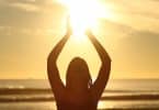 Uma mulher de braços erguidos comprimindo parte de uma luz solar forte com suas mãos.