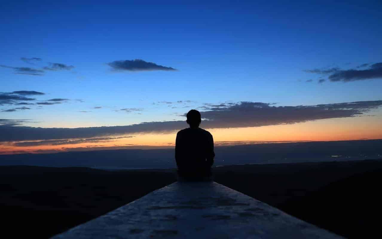 Um homem observando um poente; um pôr do sol ou um nascer do sol.