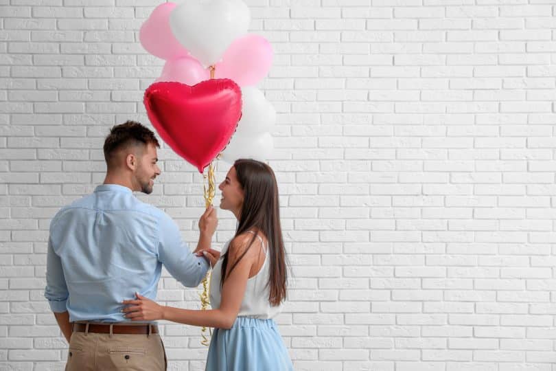 Um homem e uma mulher segurando balões em formato de coração.