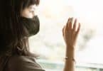 Uma mulher de máscara preta colocando sua mão direita sobre uma janela de vidro.