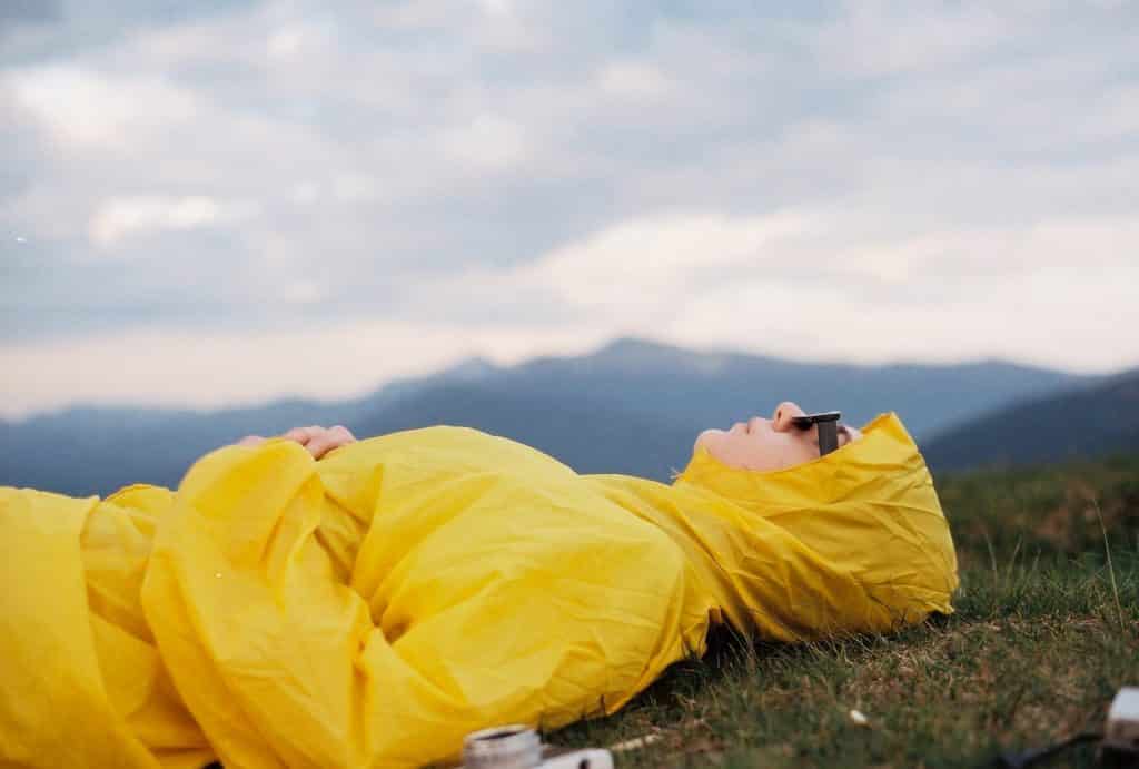 Pessoa branca deitada numa grama com capa amarela.