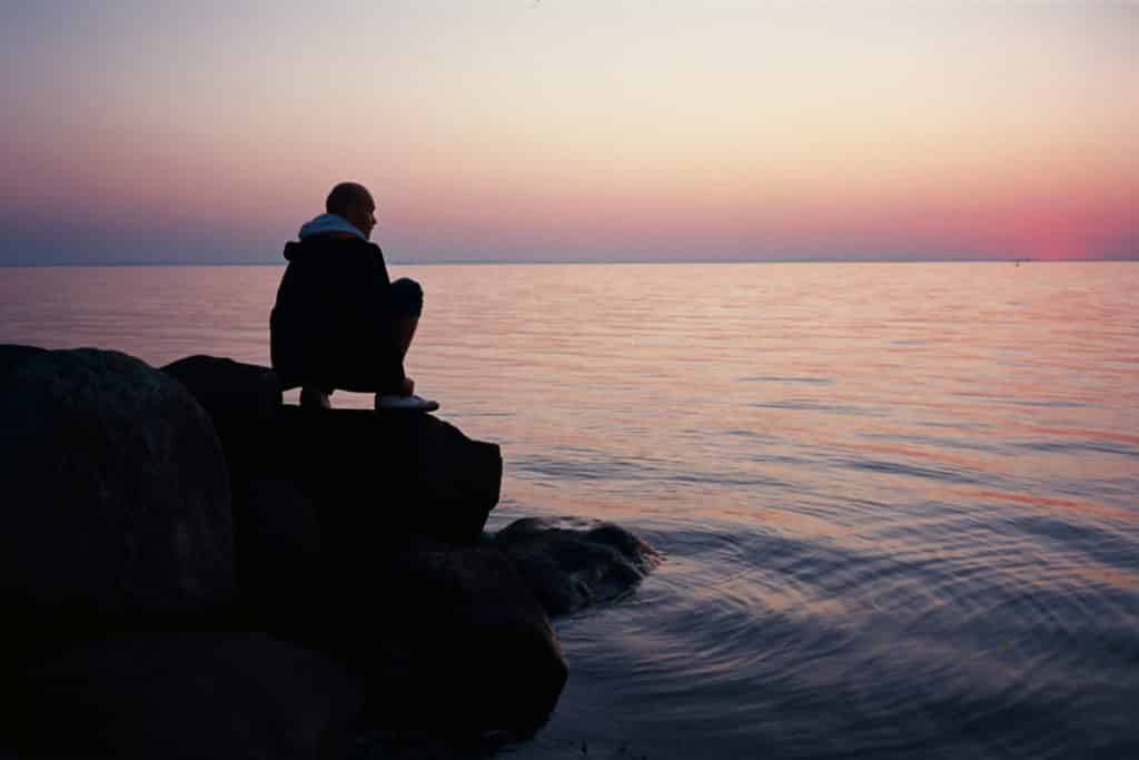 Homem agachado numa pedra próximo ao mar.