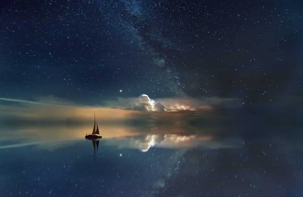 Silhueta de barco em um oceano que reflete o céu estrelado.