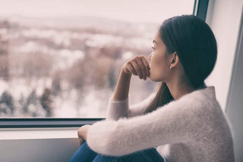 Uma mulher olhando uma paisagem através de uma janela.