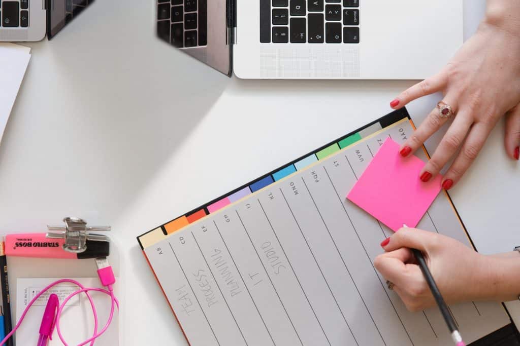 Mulher branca escrevendo em planner e post-it.