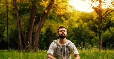 Um homem de olhos fechados com a cabeça erguida ao alto. Ele está num campo verde.