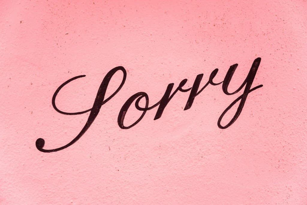 Palavra "sorry" escrito em marrom numa parede rosa.
