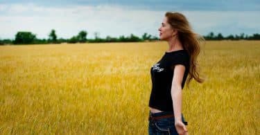 Mulher branca de braços abertos num campo.