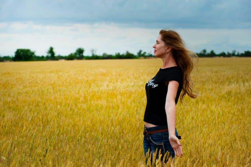 Mulher branca de braços abertos num campo.