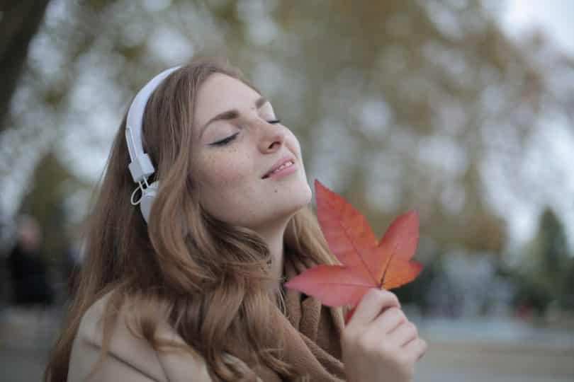 Mulher branca de fones de ouvido com os olhos fechados e segurando folha.
