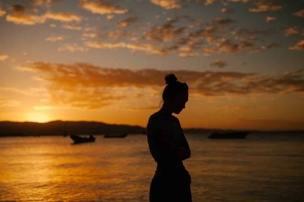 Silhueta de mulher na praia no pôr do sol.