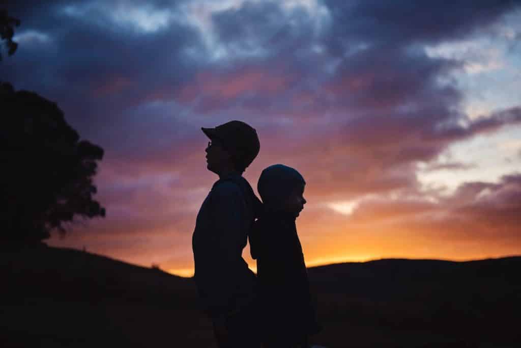 Meninos brancos de costas um para o outro e pôr-do-sol ao fundo.