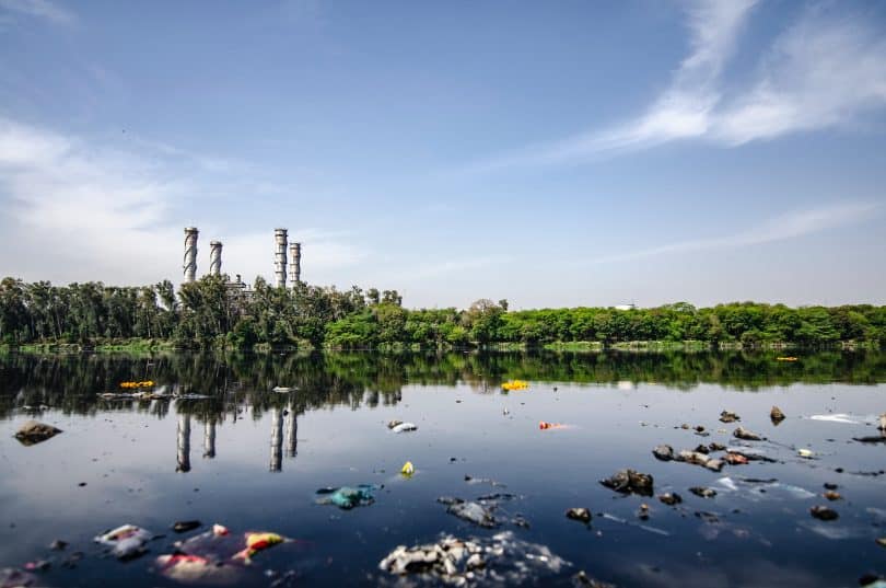 Imagem de um lago sujo em frente à uma fábrica