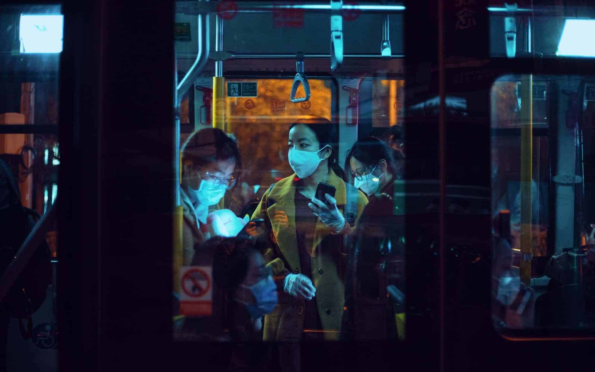 Pessoas trajadas de máscaras dentro de um ônibus.