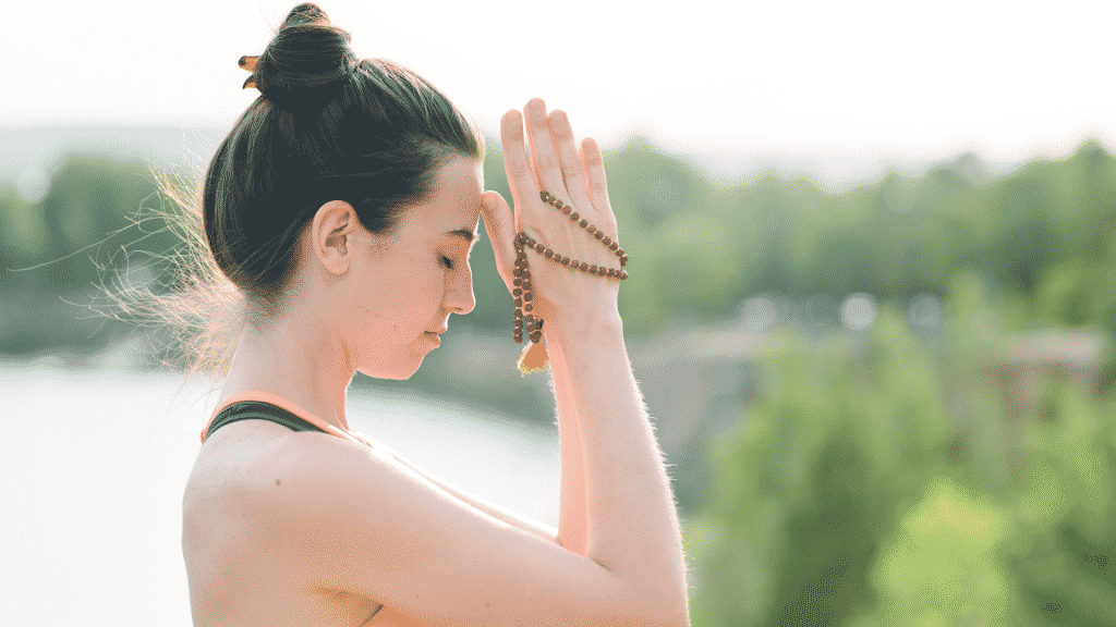 Uma mulher em gesto de oração, com as mãos sobre o rosto, segurando uma espécie de terço.