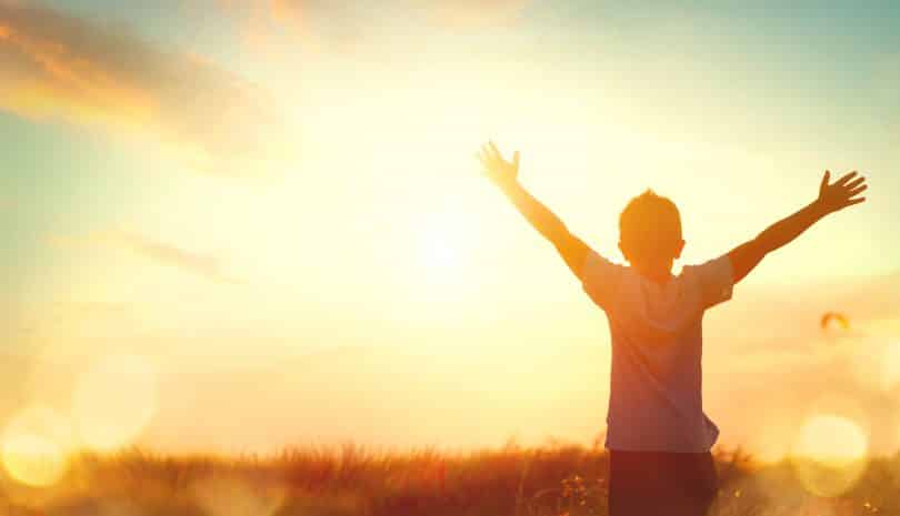 Um garoto com braços erguidos sendo ofuscado pela luz solar.