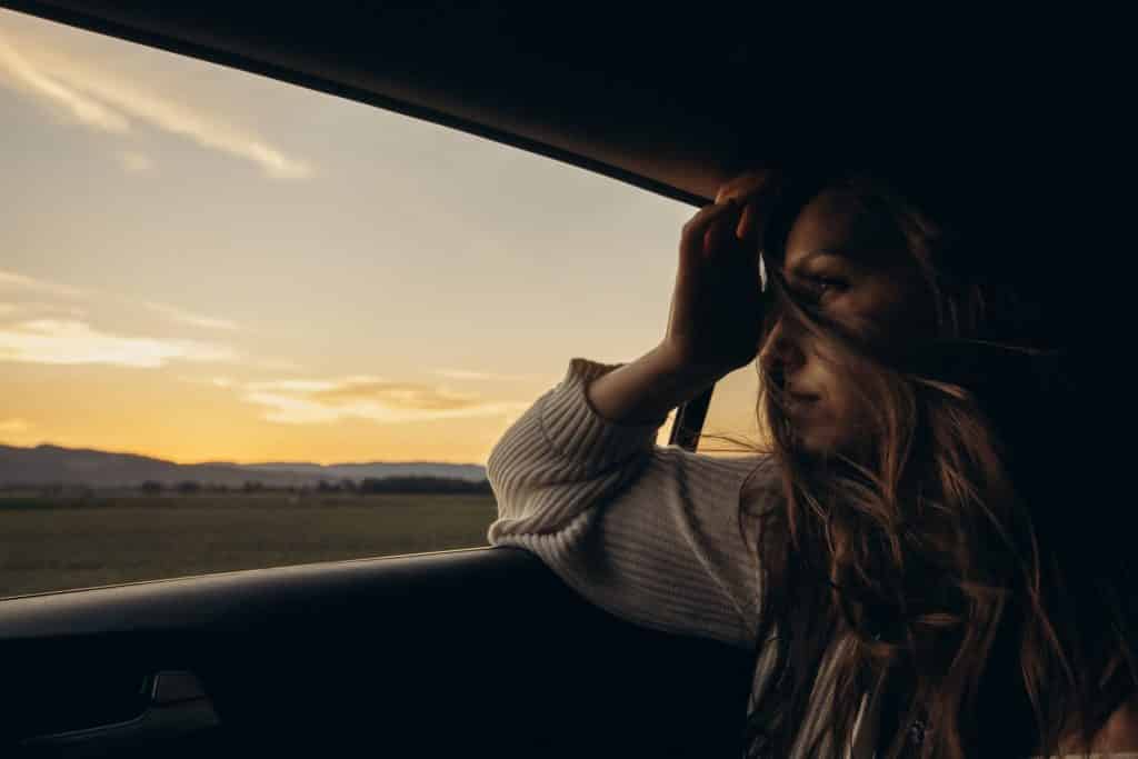 Mulher branca com cabelo no rosto dentro de um carro.