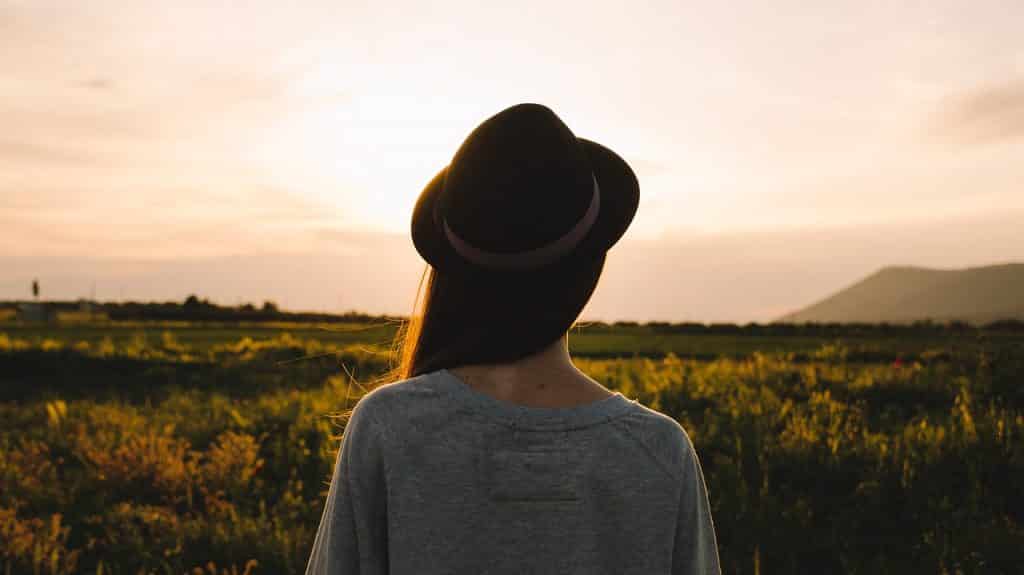 Mulher de chapéu de frente para um campo