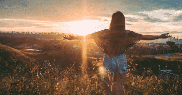 Mulher no topo da montanha com os braços estendidos observando o por do sol