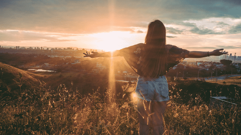 Mulher no topo da montanha com os braços estendidos observando o por do sol