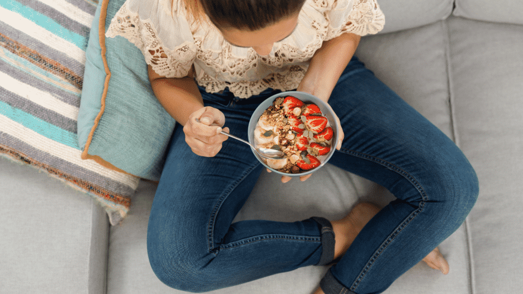 Mulher comendo tigela de frutas sentada no sofá