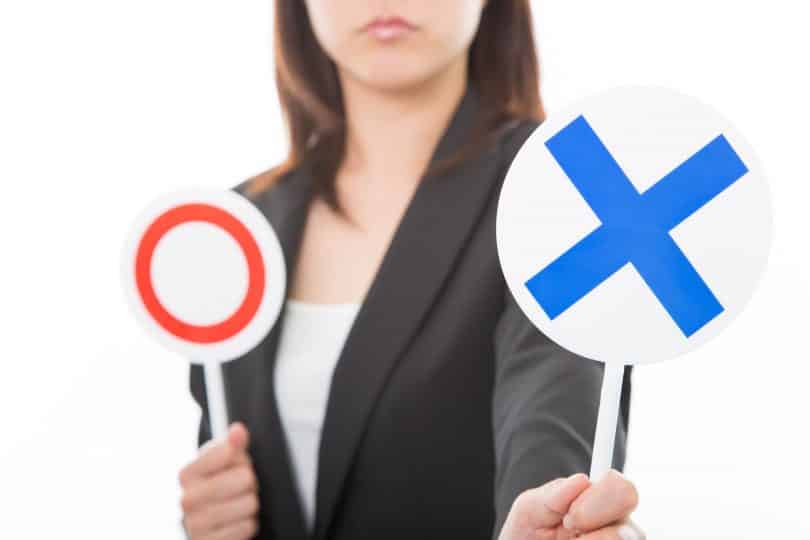 Uma mulher erguendo uma placa com um X azul. A outra placa, retida, é um círculo vermelho.